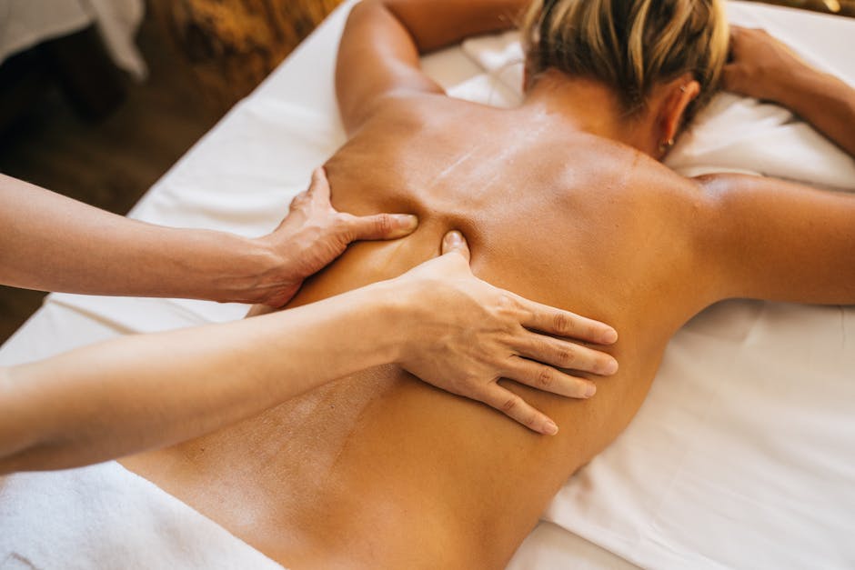 Masaż relaksacyjny wykonywany na plecach kobiety, z widoczną ręką masażysty. Tło w naturalnych odcieniach, podkreślające atmosferę spa i odprężenia.