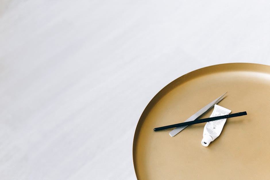 Stół o złotym blacie z nożyczkami, pędzlem i tubką farby, na jasnym tle.