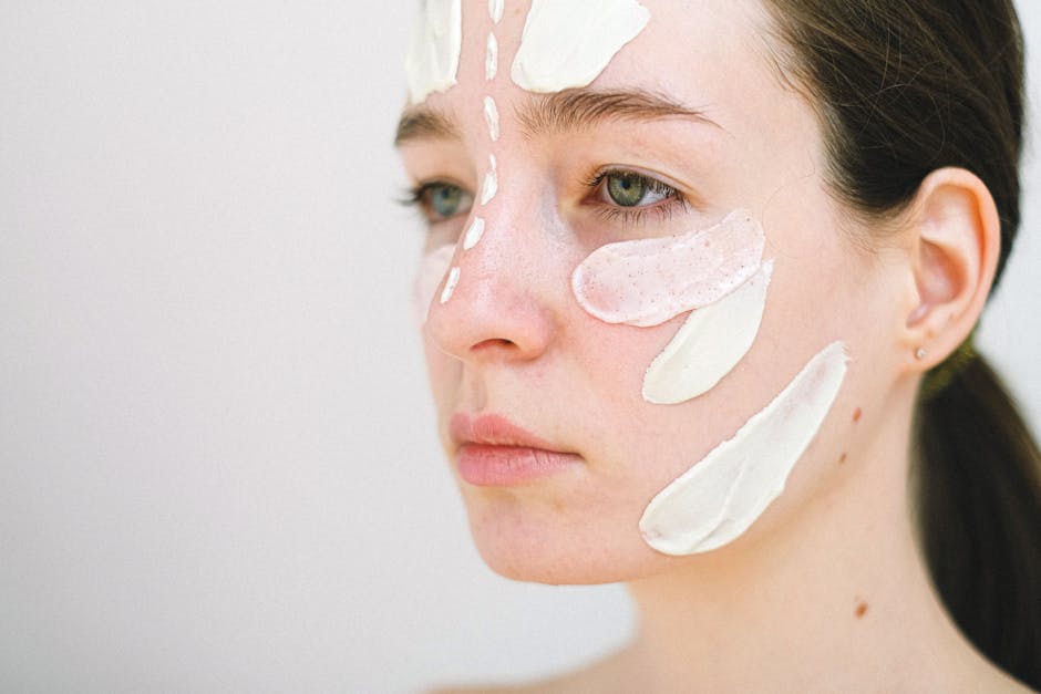 Młoda kobieta z nałożonymi różnymi rodzajami maseczek na twarz, siedząca na jasnym tle. Skupienie na pielęgnacji skóry i relaksacji.